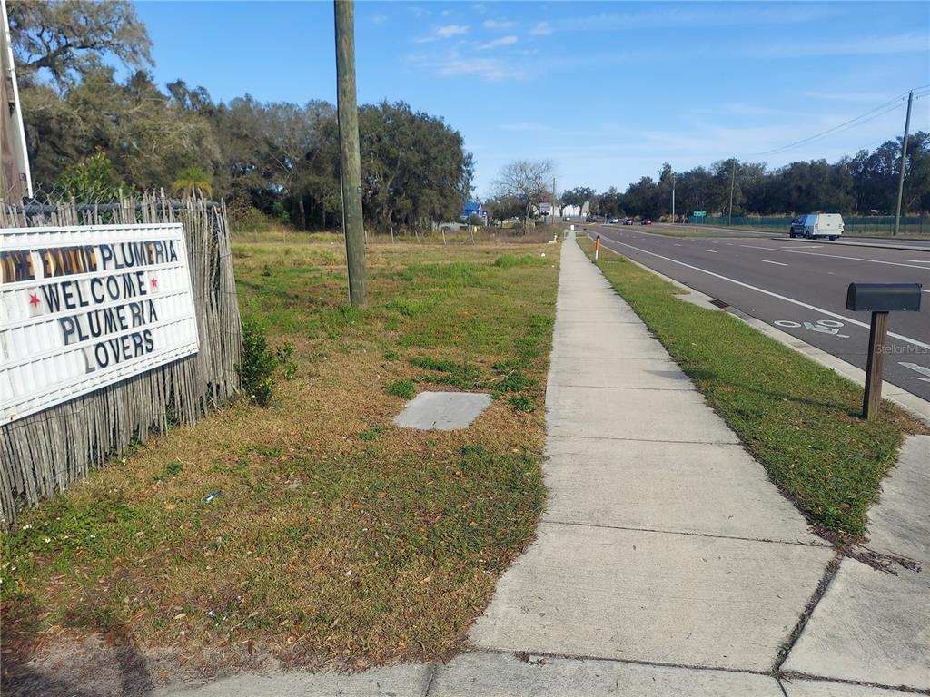 A sidewalk runs alongside a road next to a sign for a plumeria nursery — 453 W DR MARTIN LUTHER KING JR BOULEVARD, SEFFNER, FL