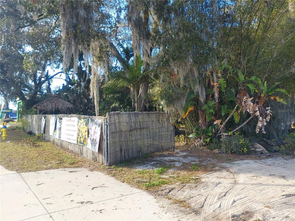 A fenced lot with trees and vegetation sits next to a sidewalk and dirt path — 453 W DR MARTIN LUTHER KING JR BOULEVARD, SEFFNER, FL