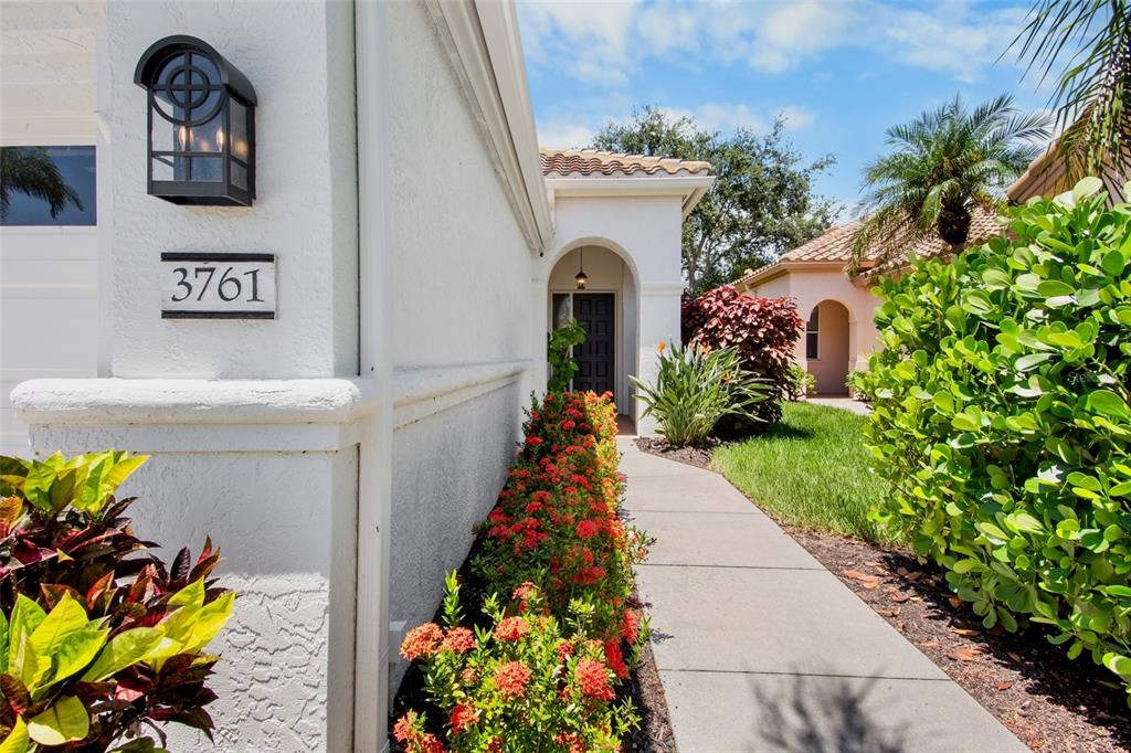 A concrete walkway leads to the arched entryway of a white stucco house with landscaping — 3761 AMAPOLA LANE, SARASOTA, FL