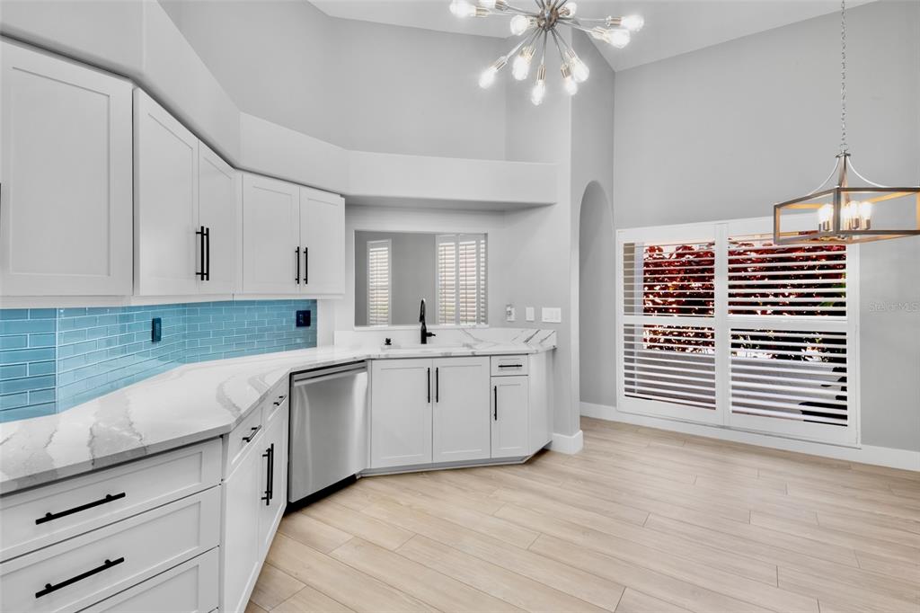 A modern kitchen features white cabinets, light wood-look flooring, a blue backsplash, and stainless appliances — 3761 AMAPOLA LANE, SARASOTA, FL