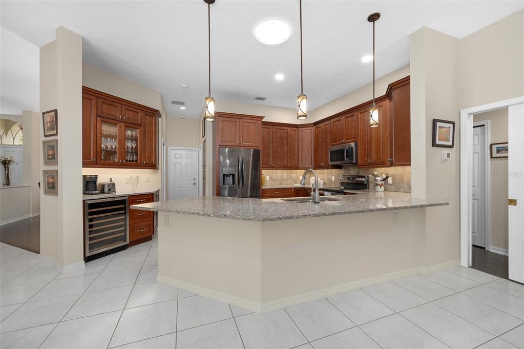 A kitchen with cherry wood cabinets, granite countertops, stainless steel appliances, and white tile flooring — 9325 SW 35TH LANE, GAINESVILLE, FL