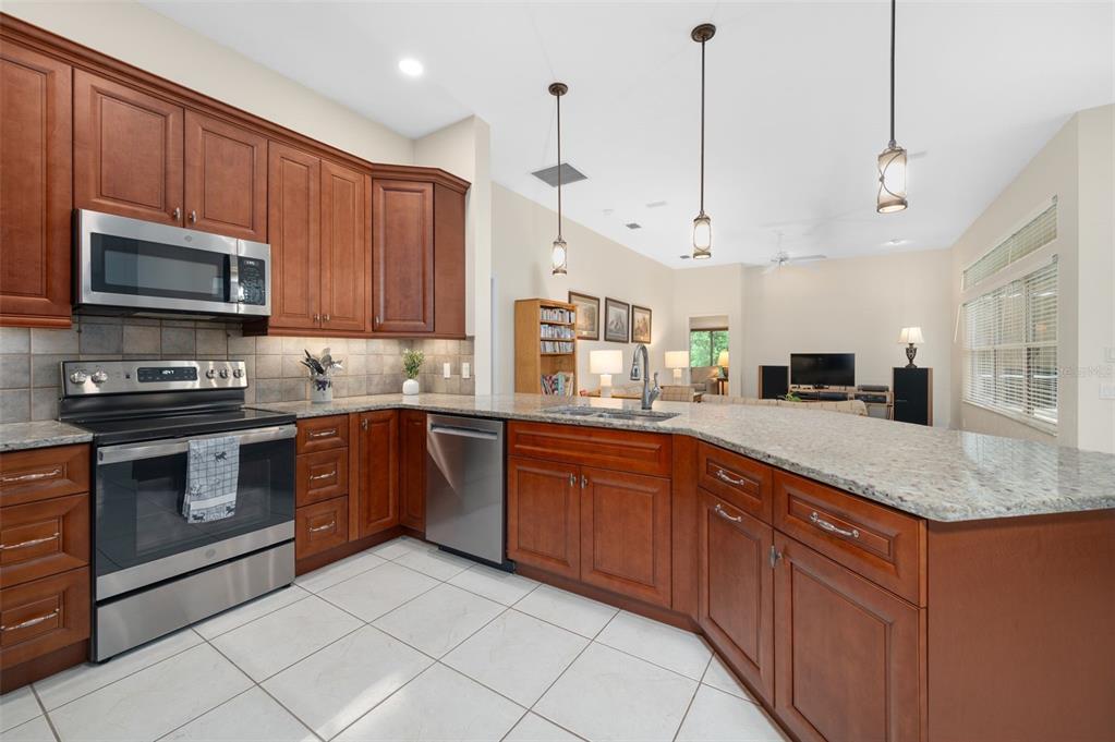 A kitchen with wood cabinets, granite countertops, and stainless steel appliances overlooks a living area — 9325 SW 35TH LANE, GAINESVILLE, FL