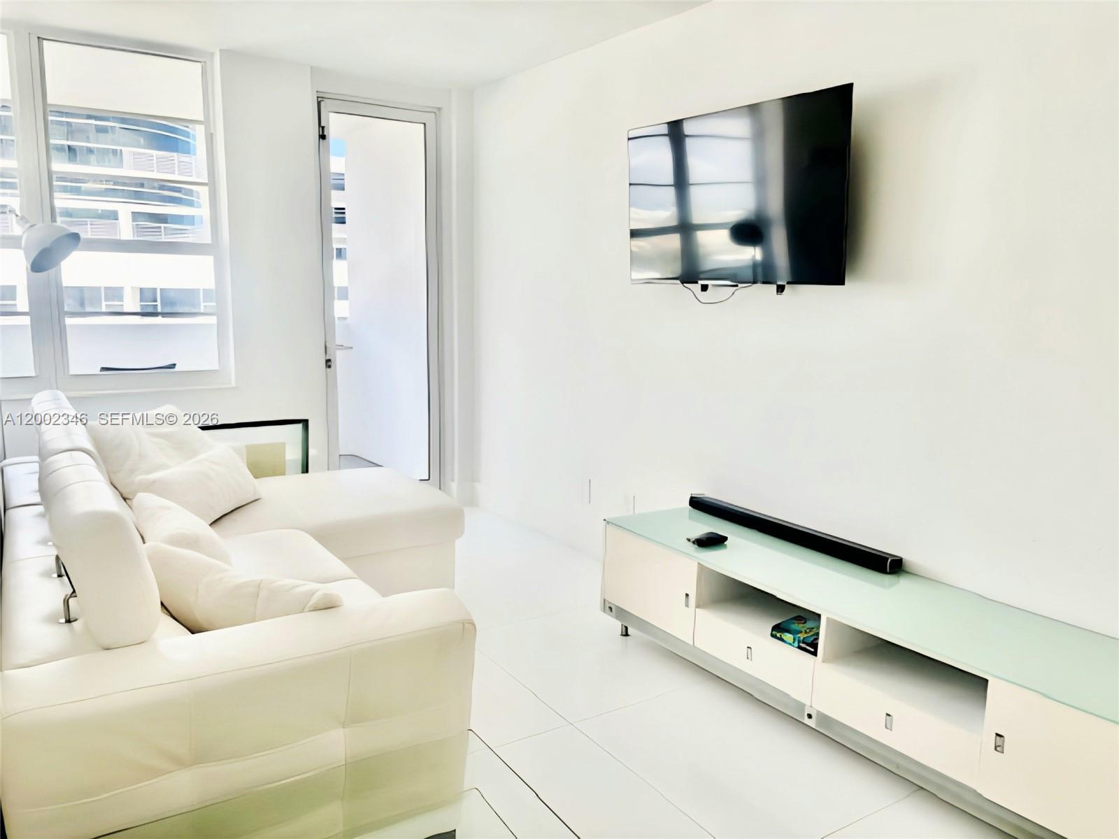 A bright living room features white furniture, a wall-mounted television, and a glass-topped media console — 100 Lincoln Rd # 927, Miami Beach FL 33139, MIAMI BEACH, FL