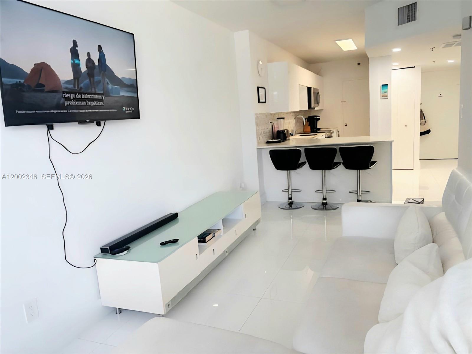 A modern living room features a wall-mounted television, white media console, and an open kitchen — 100 Lincoln Rd # 927, Miami Beach FL 33139, MIAMI BEACH, FL
