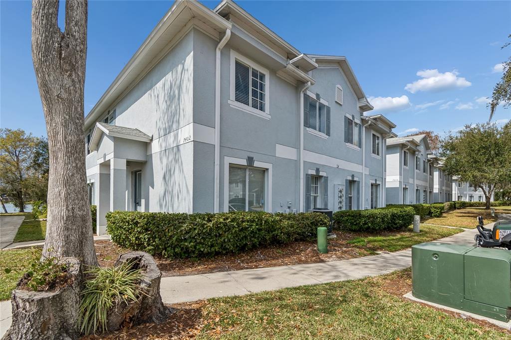 A two-story light gray apartment building with a sidewalk and landscaping in the foreground — 7402 E BANK DRIVE, TAMPA, FL