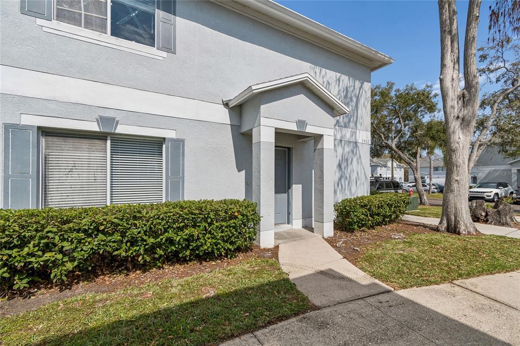 A two-story gray stucco building features a covered entryway, gray shutters, and a concrete walkway — 7402 E BANK DRIVE, TAMPA, FL