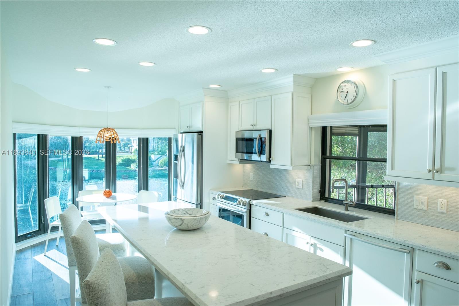 A bright kitchen features white cabinetry, a marble-topped island, and large windows overlooking water — 17081 Waterbend Dr # 227, Jupiter FL 33477, JUPITER, FL