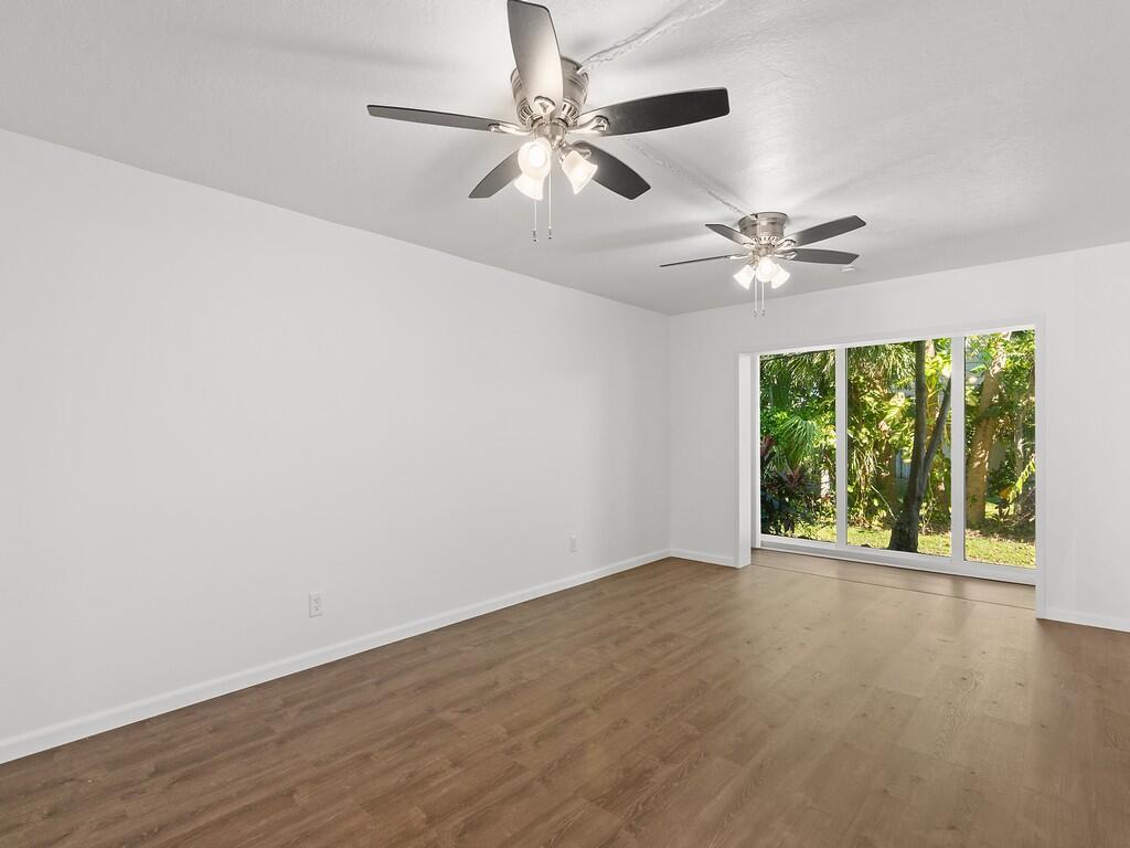 An empty room with wood-look flooring, two ceiling fans, and large sliding glass doors — 1166 6th Avenue # C5, Vero Beach FL 32960, VERO BEACH, FL