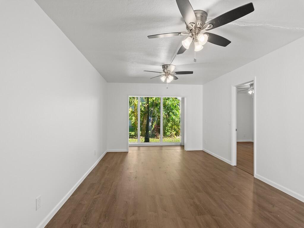 An empty room with wood-look flooring, two ceiling fans, and a large sliding glass door — 1166 6th Avenue # C5, Vero Beach FL 32960, VERO BEACH, FL