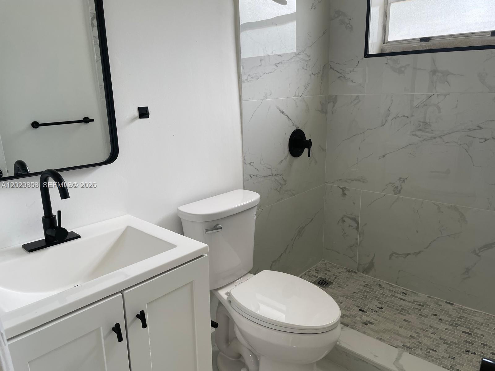A bathroom features a white vanity, a toilet, and a walk-in shower with marble-look tiles — 6021 Polk St # 4, Hollywood FL 33024, HOLLYWOOD, FL