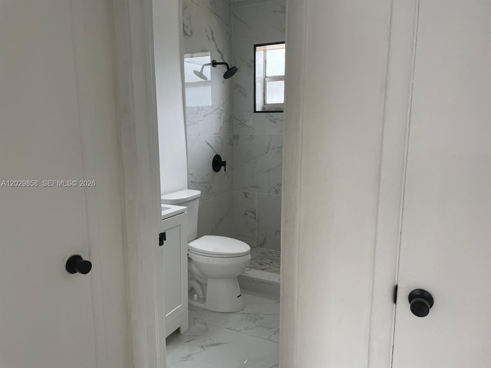 A bathroom features white marble-look tile, a white toilet, and matte black fixtures — 6021 Polk St # 4, Hollywood FL 33024, HOLLYWOOD, FL