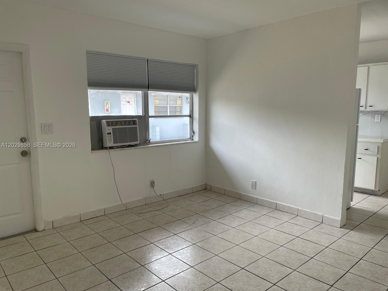This room features white walls, tiled flooring, a window air conditioning unit, and an adjacent kitchen — 6021 Polk St # 4, Hollywood FL 33024, HOLLYWOOD, FL