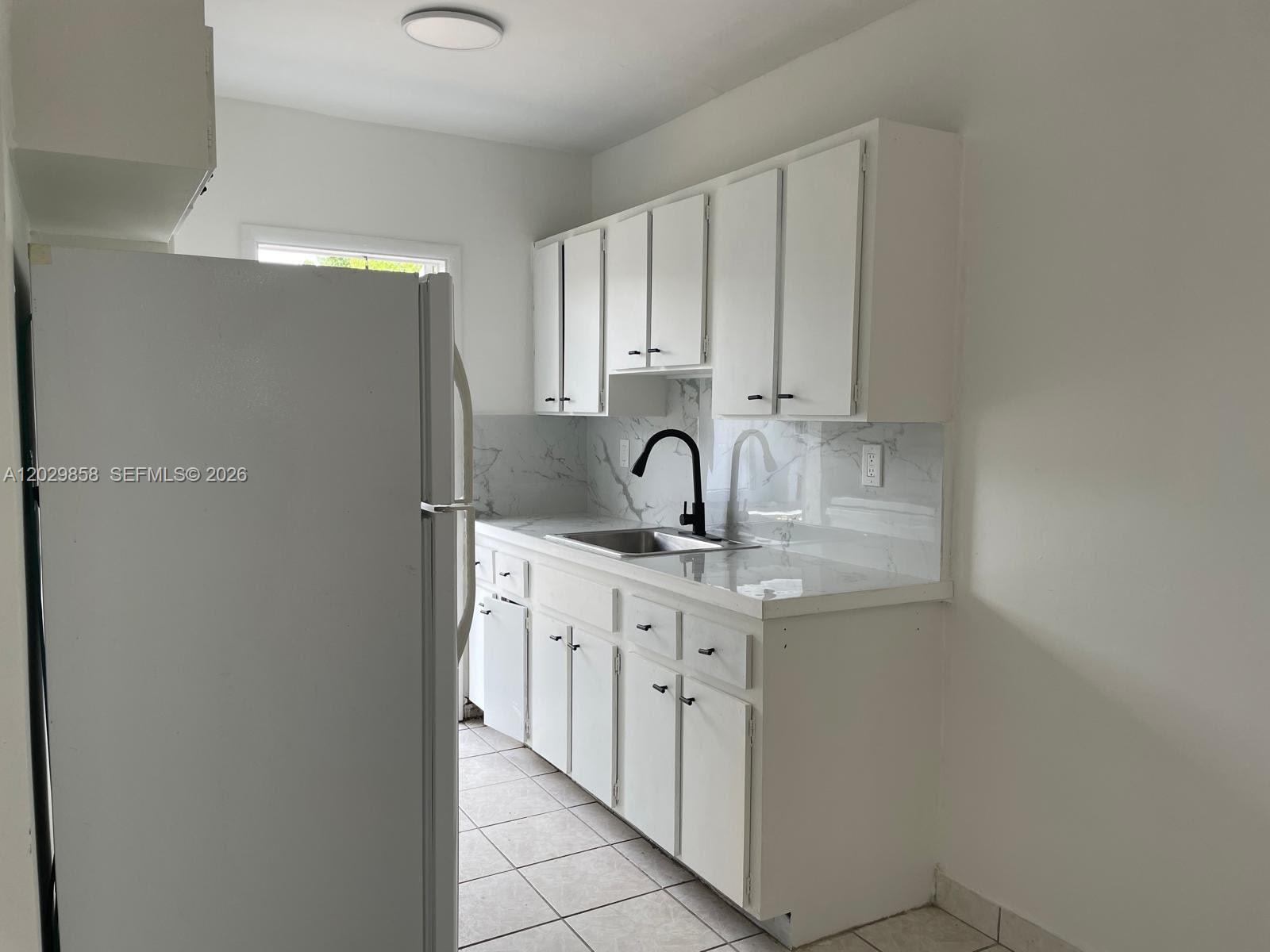 A kitchen features white cabinets, marble-patterned countertops, a black faucet, and light tile flooring — 6021 Polk St # 4, Hollywood FL 33024, HOLLYWOOD, FL