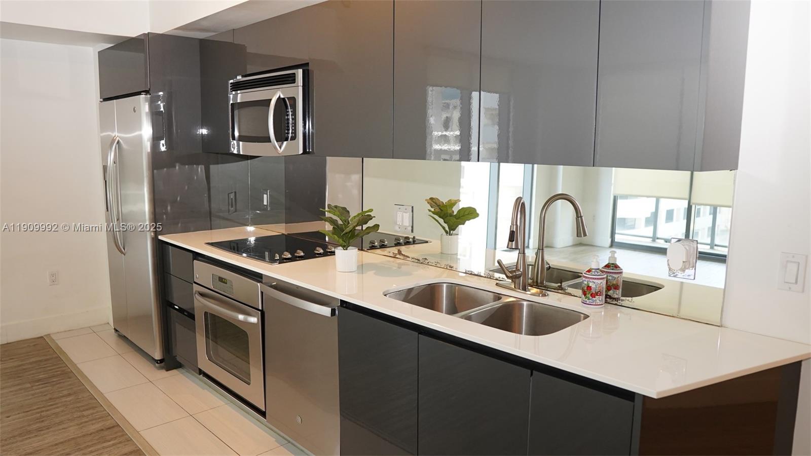 A modern kitchen features dark gray cabinets, stainless steel appliances, and a mirrored backsplash — 31 SE 6th St # 1108, Miami FL 33131, MIAMI, FL
