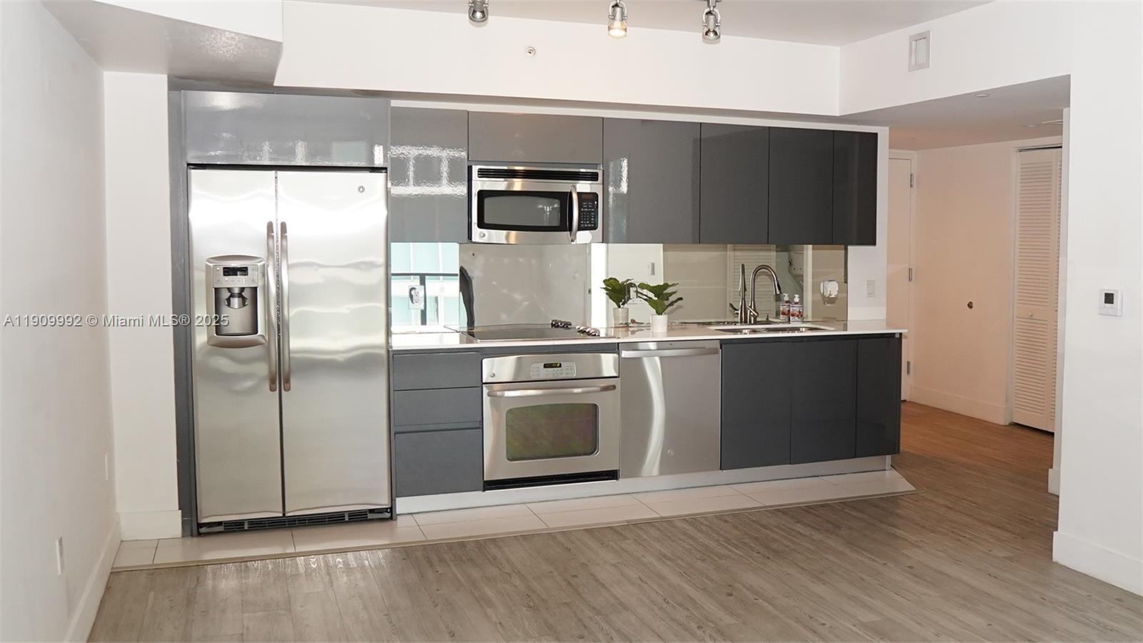 A modern kitchen features stainless steel appliances, dark gray cabinetry, and a mirrored backsplash — 31 SE 6th St # 1108, Miami FL 33131, MIAMI, FL