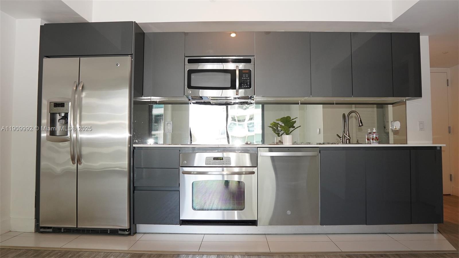 A modern kitchen features stainless steel appliances, dark gray cabinetry, and a mirrored backsplash — 31 SE 6th St # 1108, Miami FL 33131, MIAMI, FL