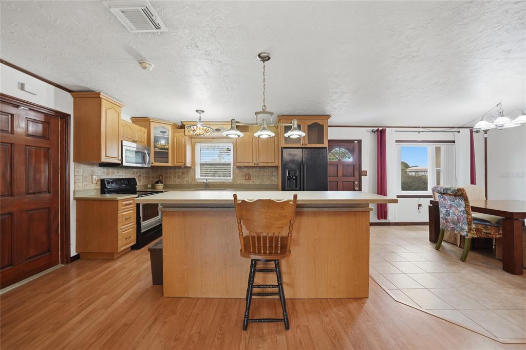 A kitchen features light wood cabinets, a central island with a stool, and tile flooring — 3250 SANTA BARBARA DRIVE, PUNTA GORDA, FL