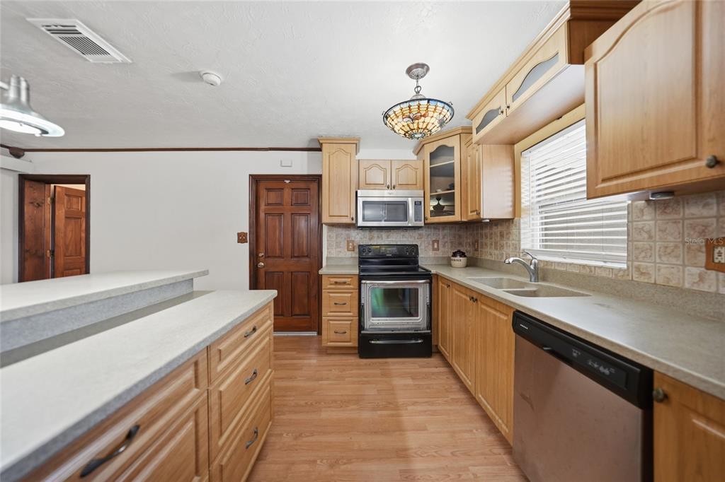 A kitchen features light wood cabinets, laminate countertops, stainless steel appliances, and wood-look flooring — 3250 SANTA BARBARA DRIVE, PUNTA GORDA, FL