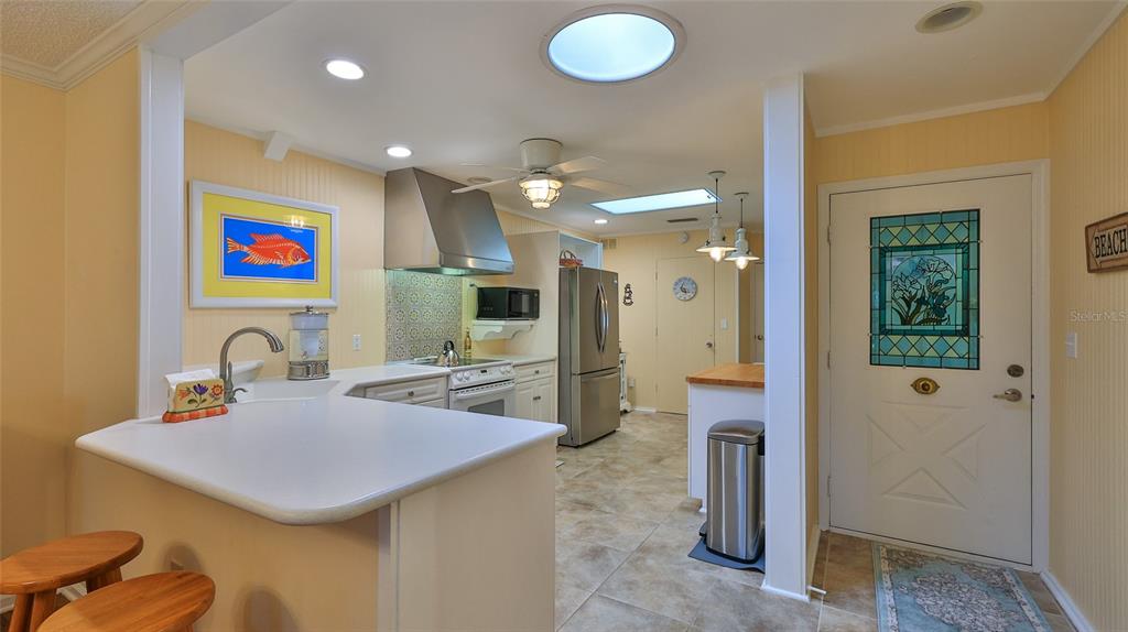 A kitchen with white cabinets, stainless steel appliances, and a breakfast bar near an entryway — 25 ANDREA DRIVE, NEW SMYRNA BEACH, FL
