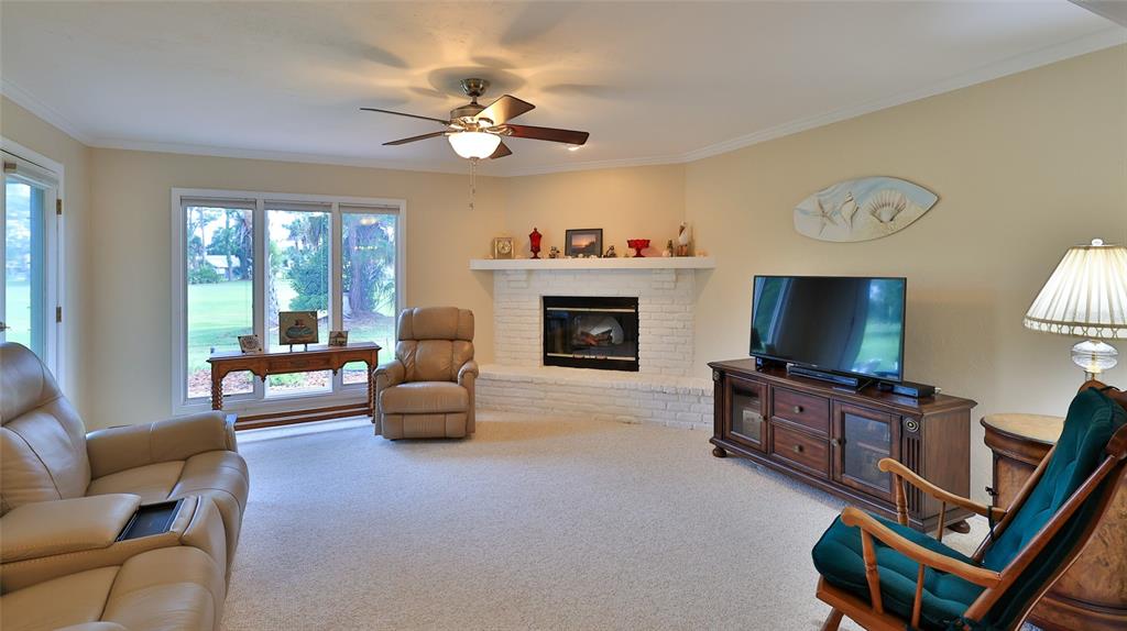 A living room features a white brick fireplace, beige carpet, and a ceiling fan — 25 ANDREA DRIVE, NEW SMYRNA BEACH, FL