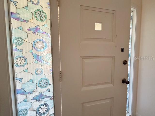 A white front door with a decorative dolphin-patterned stained glass sidelight — 121 E PINE ST, HOWEY IN THE HILLS, FL
