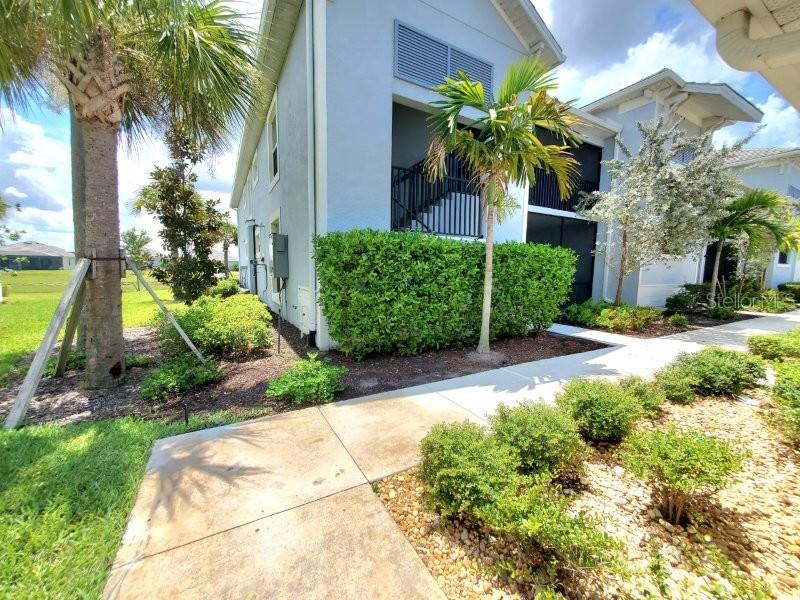 A light blue multi-story building features a manicured hedge, palm trees, and a concrete walkway — 14194 HERITAGE LANDING BOULEVARD UNIT 611, PUNTA GORDA, FL