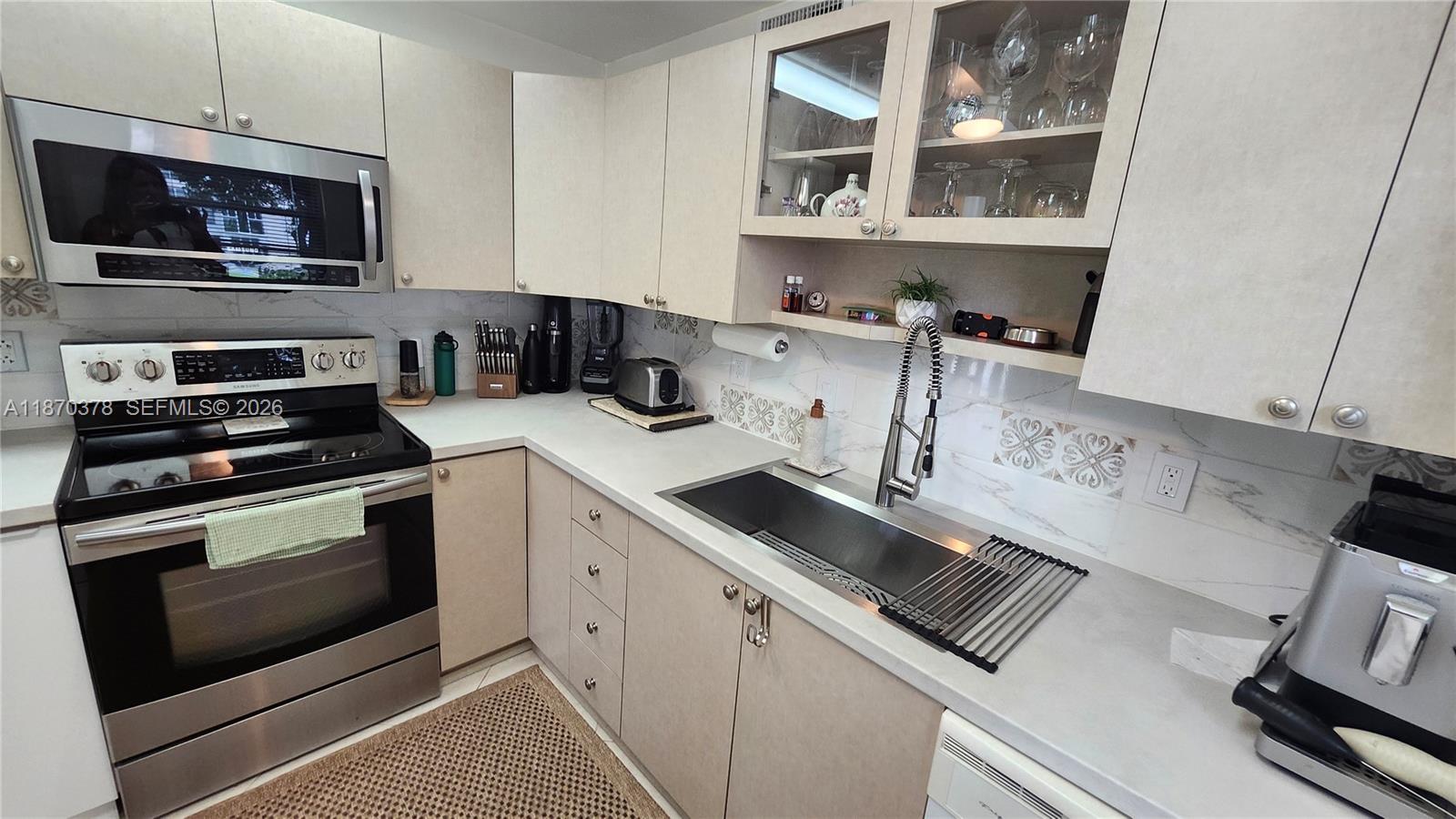 A kitchen features light-colored cabinets, stainless steel appliances, a deep sink, and marble-patterned backsplash tiles — 2001 Ventnor G # 2001, Deerfield Beach FL 33442, DEERFIELD BEACH, FL