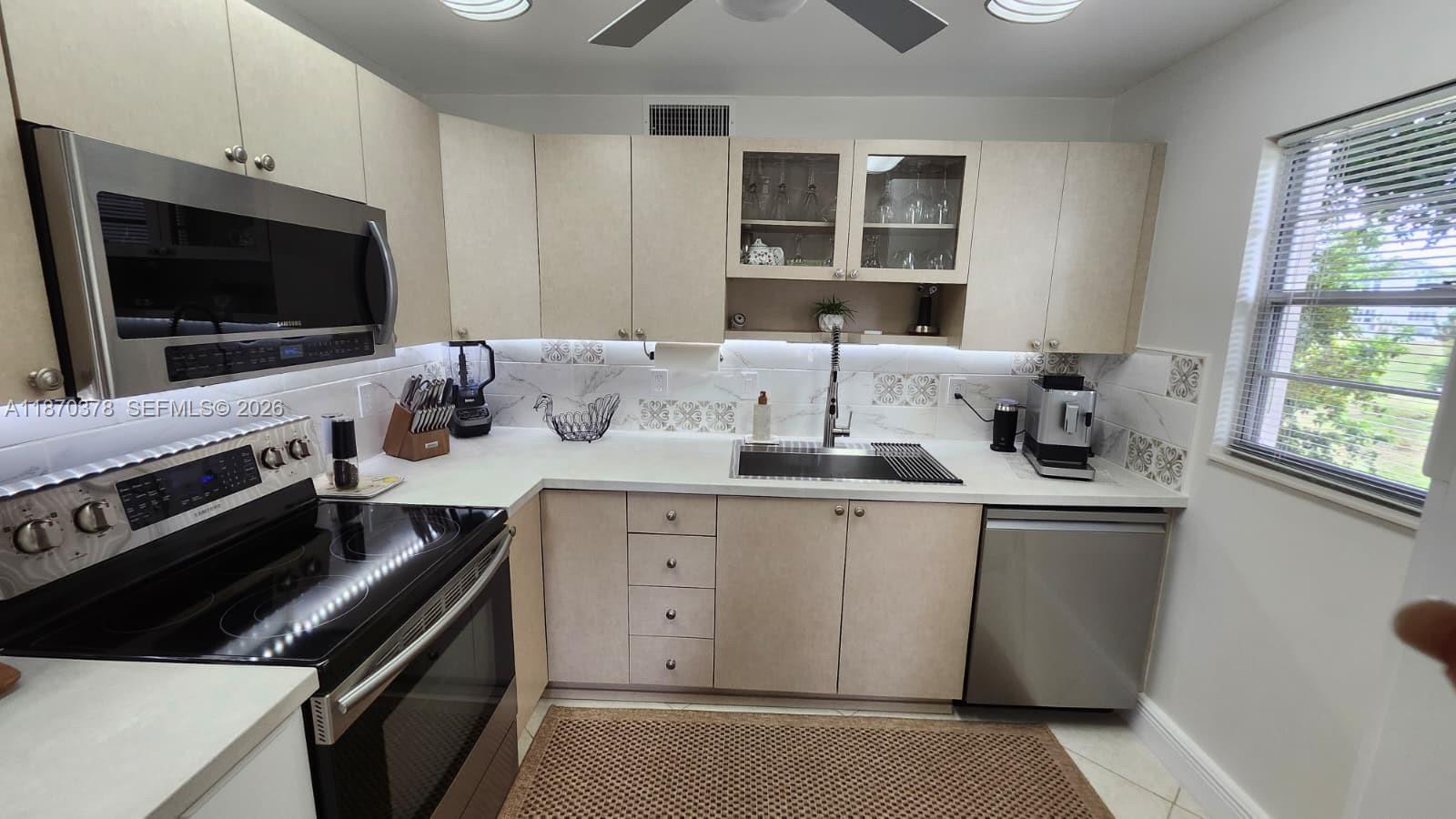 A kitchen features light wood cabinets, stainless steel appliances, and a white marble-patterned backsplash — 2001 Ventnor G # 2001, Deerfield Beach FL 33442, DEERFIELD BEACH, FL