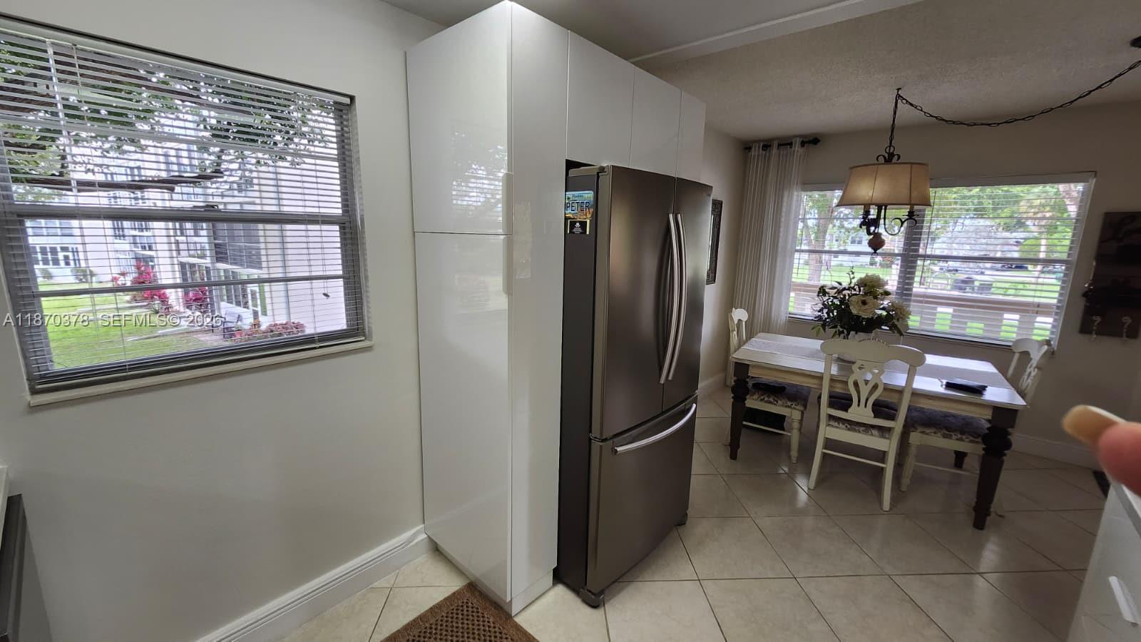 A stainless steel refrigerator is built into a white cabinet unit next to a dining area — 2001 Ventnor G # 2001, Deerfield Beach FL 33442, DEERFIELD BEACH, FL