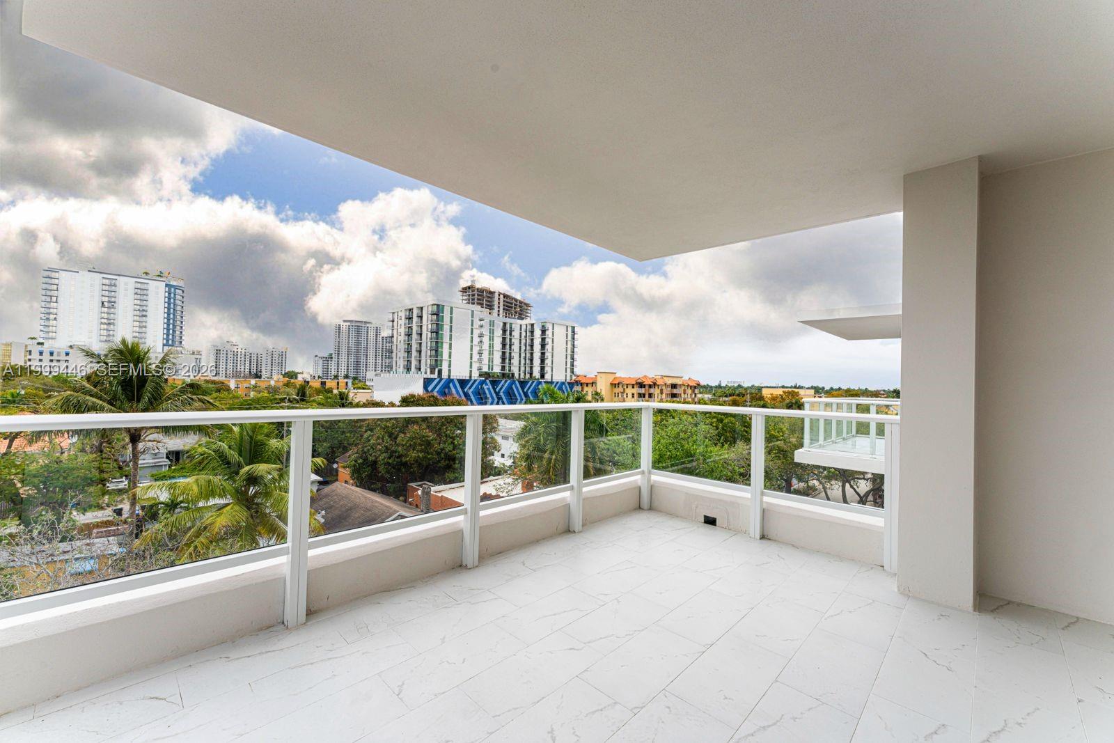 A balcony with white tiled flooring and a glass railing overlooks a city skyline — 1850 Monroe St # 403, Hollywood FL 33020, HOLLYWOOD, FL