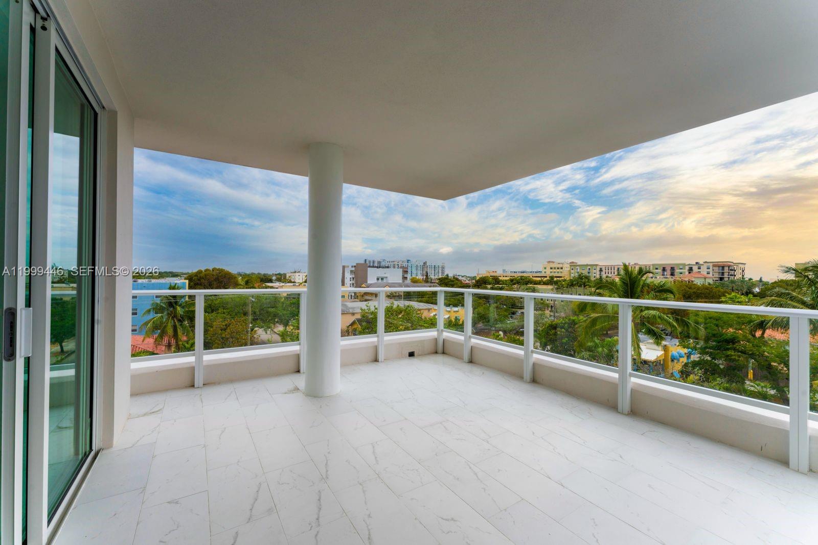 A balcony with white marble-look tile flooring, a central support column, and glass railings — 1850 Monroe St # 403, Hollywood FL 33020, HOLLYWOOD, FL