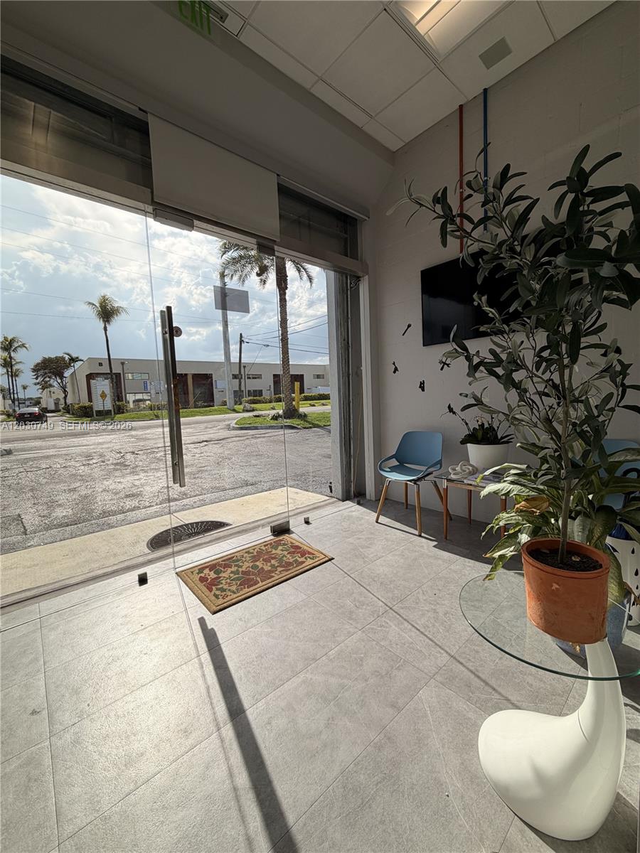 A bright office entryway features a glass door, tiled floors, a potted plant, and seating — 4705 SW 74th Ave, Miami FL 33155, MIAMI, FL