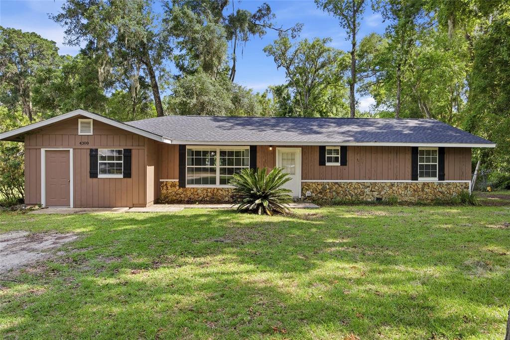 A single-story house with brown vertical siding, a stone base, and a dark shingled roof — 4300 NE 132ND PLACE, ANTHONY, FL
