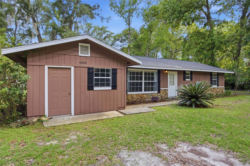 A single-story house with brown vertical siding, stone accents, and a front-facing utility door — 4300 NE 132ND PLACE, ANTHONY, FL