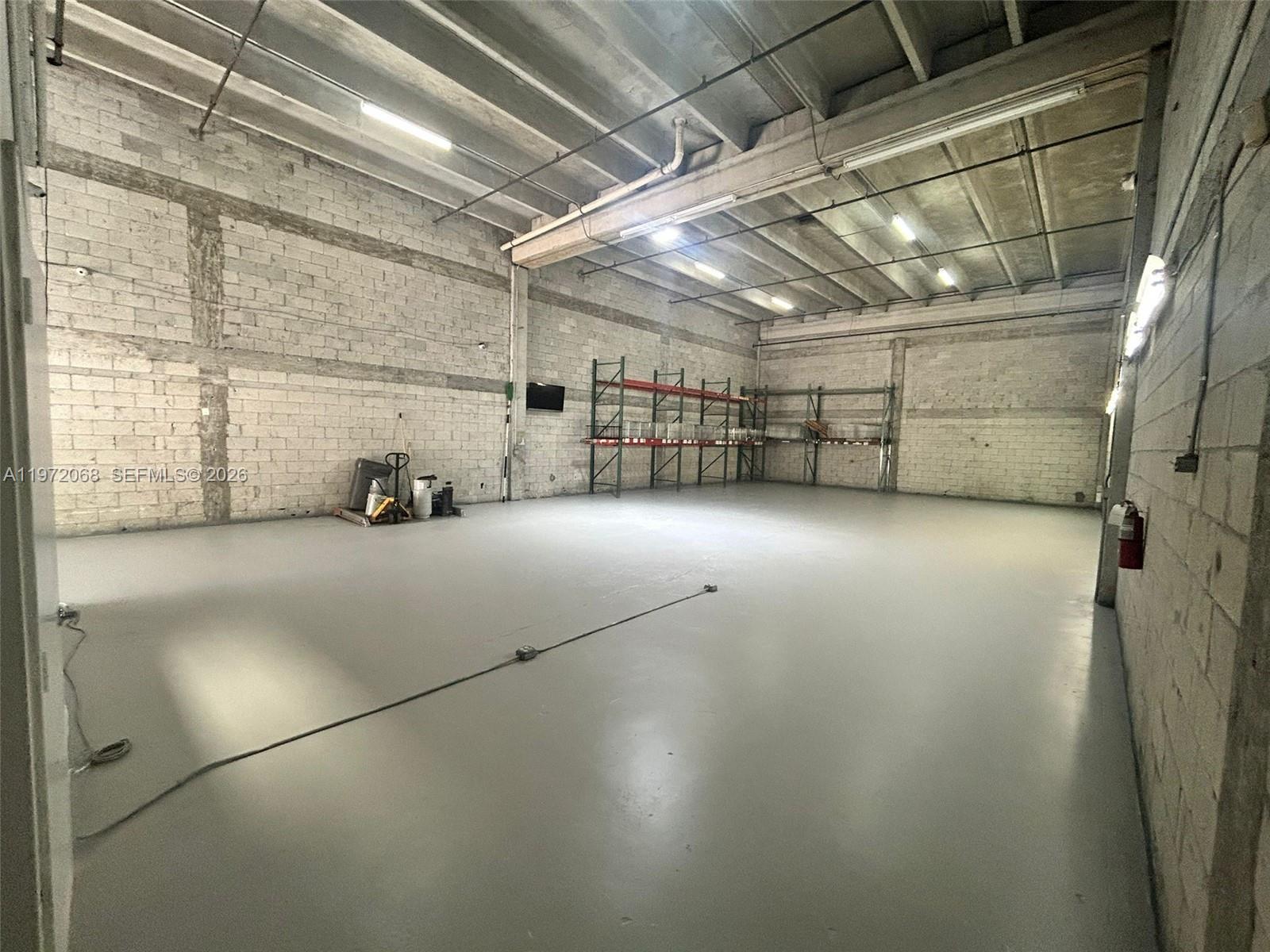 An empty industrial warehouse space features concrete block walls, a gray epoxy floor, and shelving — 6910 NW 50th St # 1, Miami FL 33195, MIAMI, FL