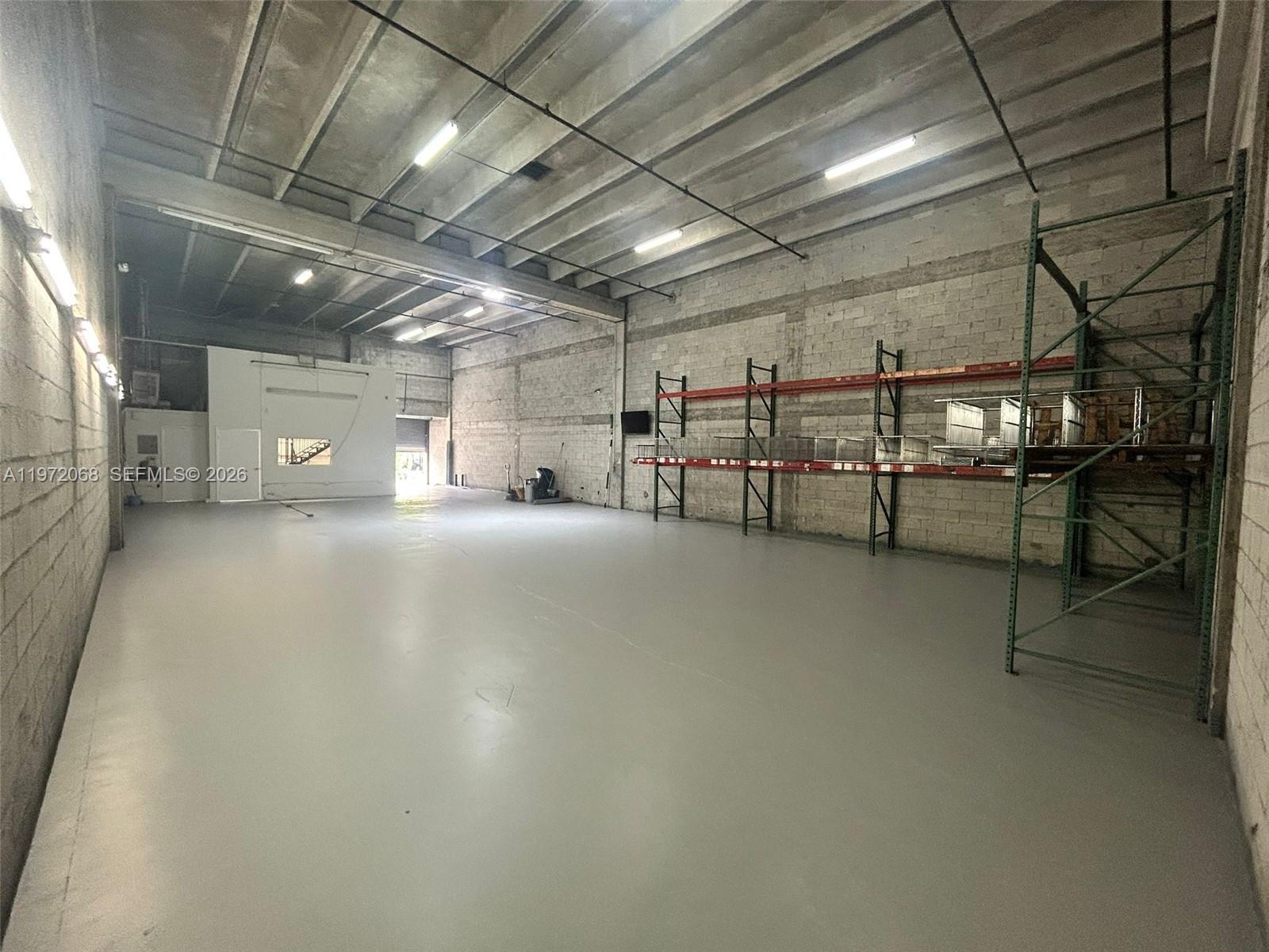 An empty industrial warehouse space features concrete block walls, a gray floor, and metal shelving — 6910 NW 50th St # 1, Miami FL 33195, MIAMI, FL