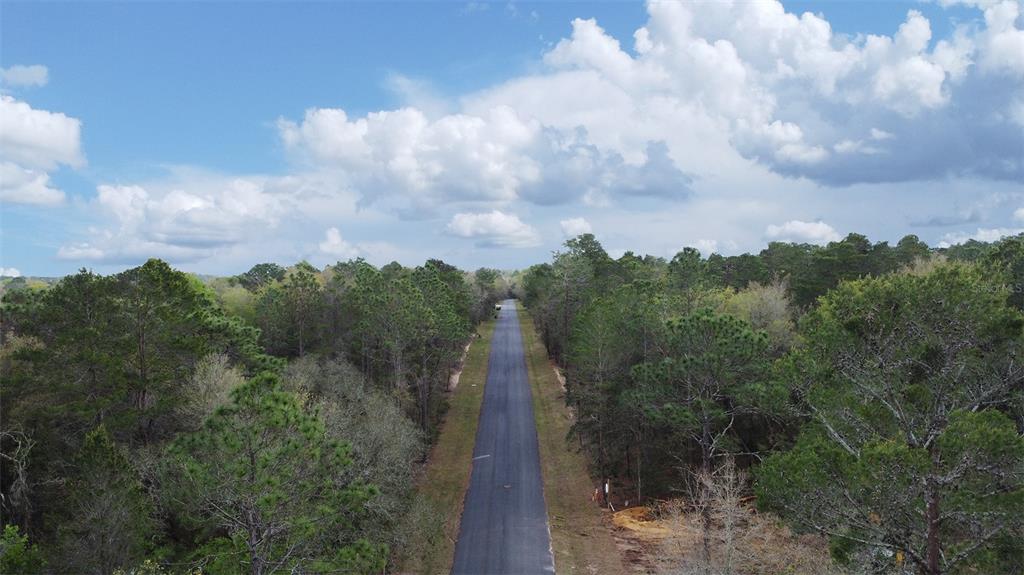 An aerial view shows a paved road stretching through a dense, wooded forest under clouds — 2612 SHEPHARD STREET, INVERNESS, FL