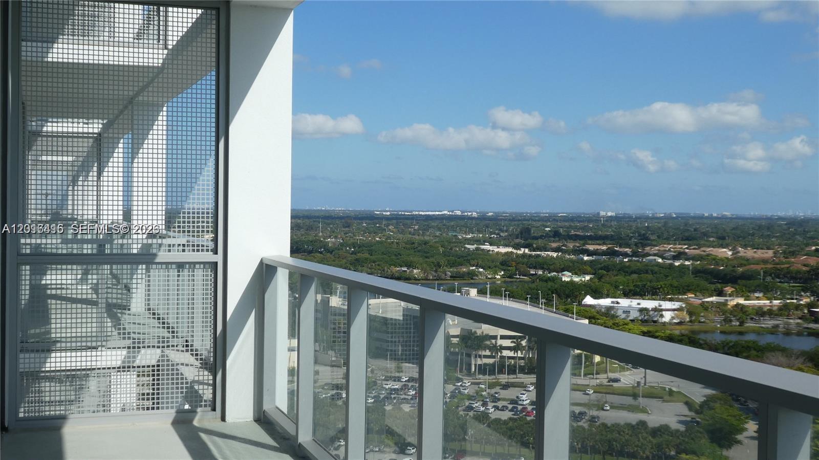 A high-rise balcony with a glass railing overlooks a suburban landscape under a blue sky — 2000 Metropica Way # 2006, Sunrise FL 33323, SUNRISE, FL