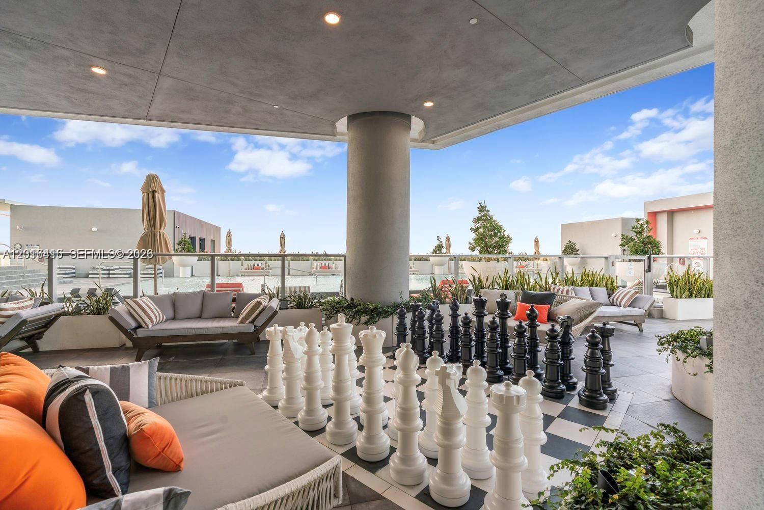 An outdoor rooftop lounge features a giant chess set, lounge seating, and a swimming pool — 2000 Metropica Way # 2006, Sunrise FL 33323, SUNRISE, FL