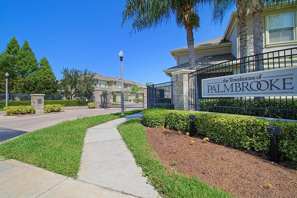 A gated entrance with a sign for The Townhomes of Palmbrooke and a paved walkway — 6648 83RD AVENUE N, PINELLAS PARK, FL