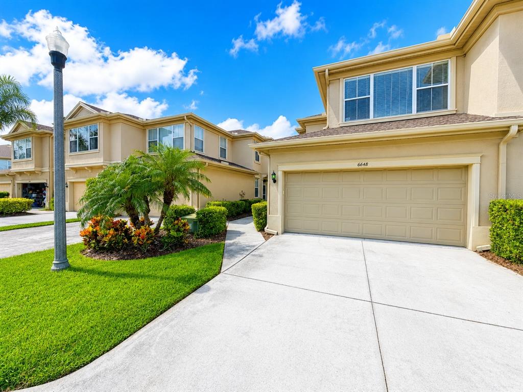A two-story tan townhouse features a two-car garage and a landscaped front yard — 6648 83RD AVENUE N, PINELLAS PARK, FL