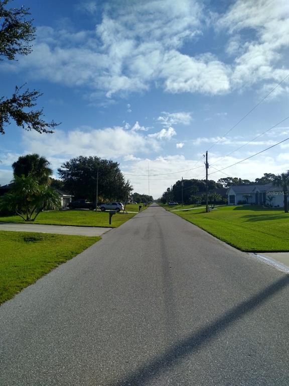A paved residential street stretches into the distance between houses with green lawns and trees — 81 LONG MEADOW PLACE, ROTONDA WEST, FL
