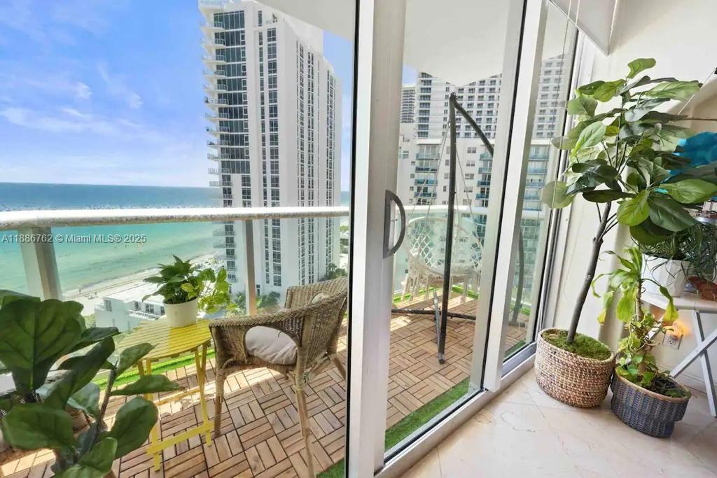 A balcony with a wicker chair and small table overlooks the ocean and nearby buildings — 3901 S Ocean Dr # 14L, Hollywood FL 33019, HOLLYWOOD, FL