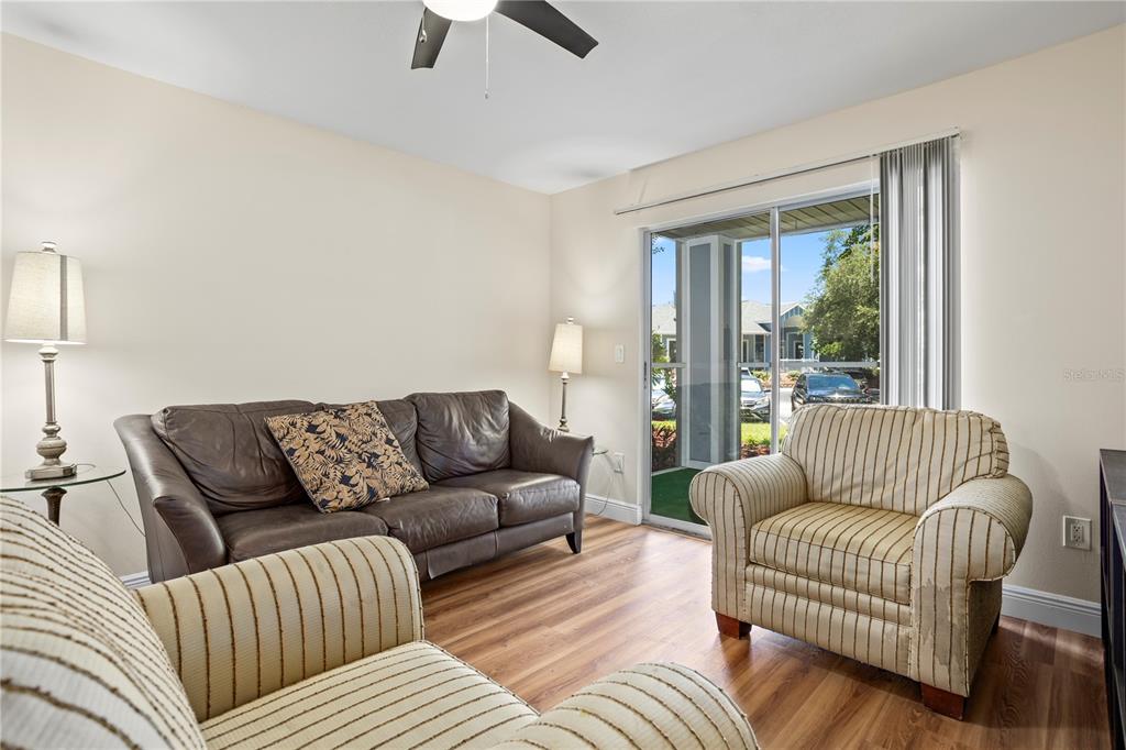 A living room features a brown leather sofa, two striped armchairs, and a sliding glass door — 2504 GRASSY POINT DRIVE UNIT 100, LAKE MARY, FL