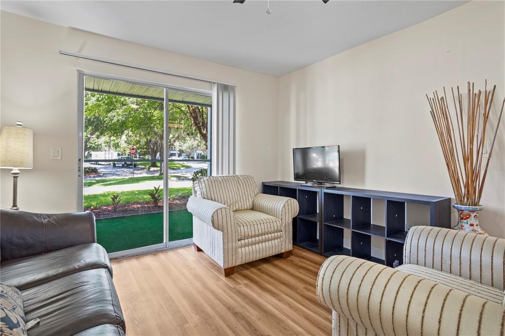 A living room features light wood flooring, striped armchairs, a dark shelving unit, and sliding doors — 2504 GRASSY POINT DRIVE UNIT 100, LAKE MARY, FL