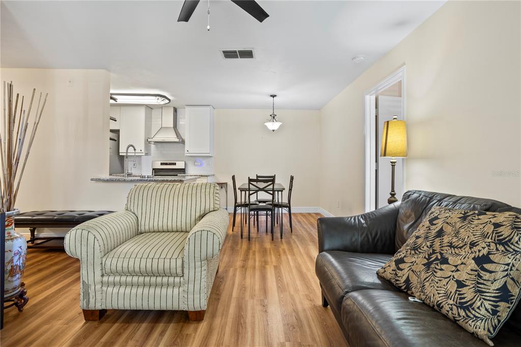 A living room with wood-look flooring leads to an open dining area and kitchen — 2504 GRASSY POINT DRIVE UNIT 100, LAKE MARY, FL