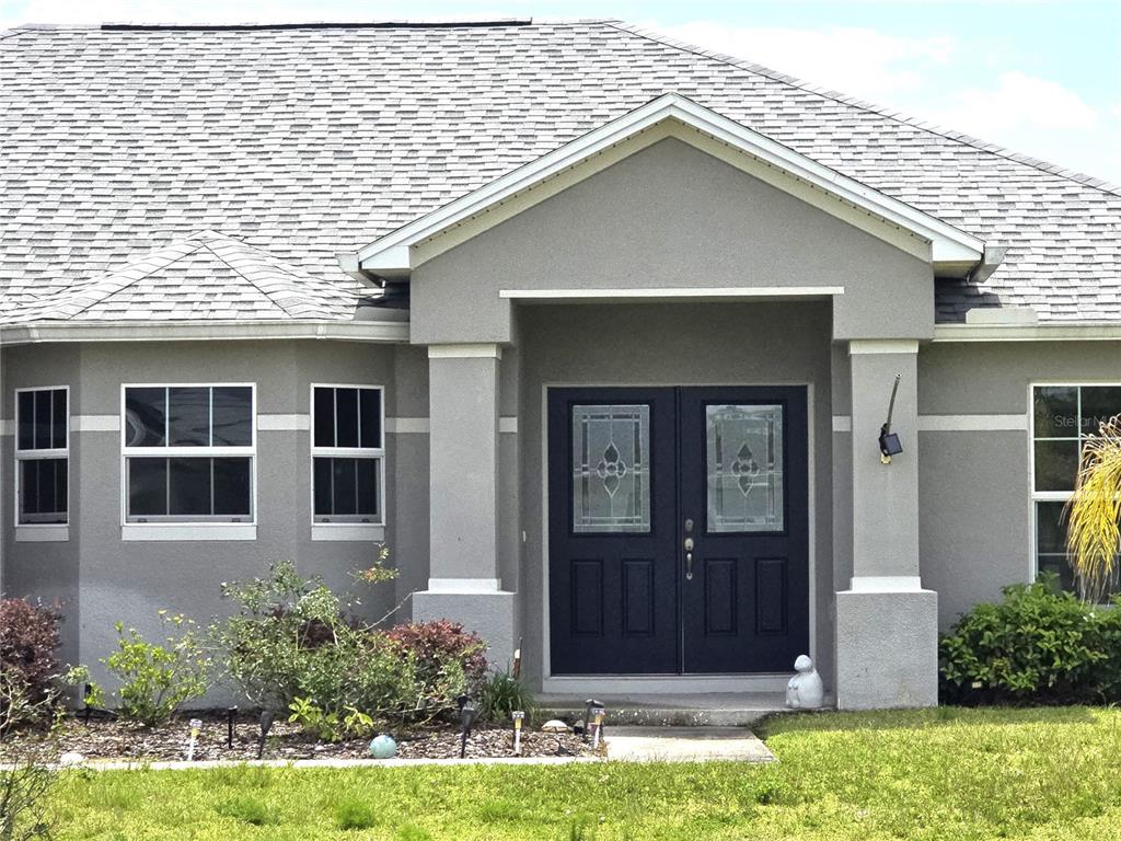 The exterior of a gray house features a double front door and a shingled roof — 4823 SAN IGNACIO DRIVE, SEBRING, FL