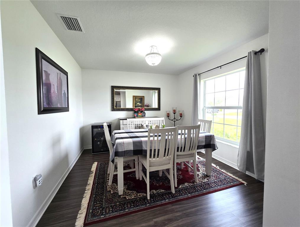 A dining room features a table with white chairs, a dark rug, and a mirror — 4823 SAN IGNACIO DRIVE, SEBRING, FL