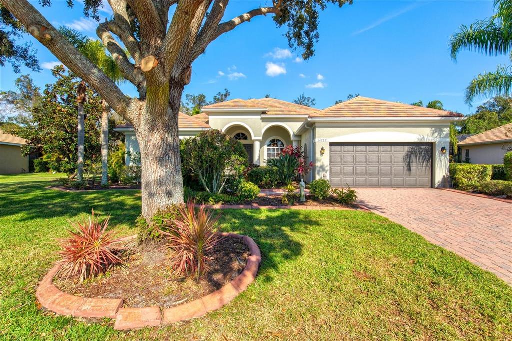 A single-story house with a tiled roof, a two-car garage, and a large front tree — 14757 2ND AVENUE CIRCLE NE, BRADENTON, FL