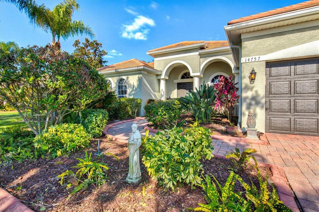 The exterior of a single-story house features a brick walkway, landscaping, and a garage — 14757 2ND AVENUE CIRCLE NE, BRADENTON, FL